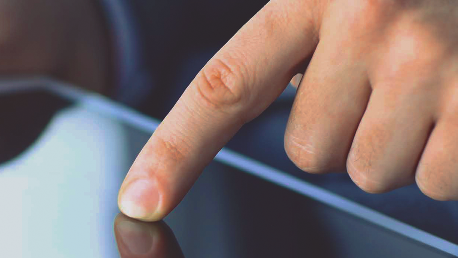 A finger in a suit touches the screen of a tablet or smartphone, whose surface reflects the image of the finger.