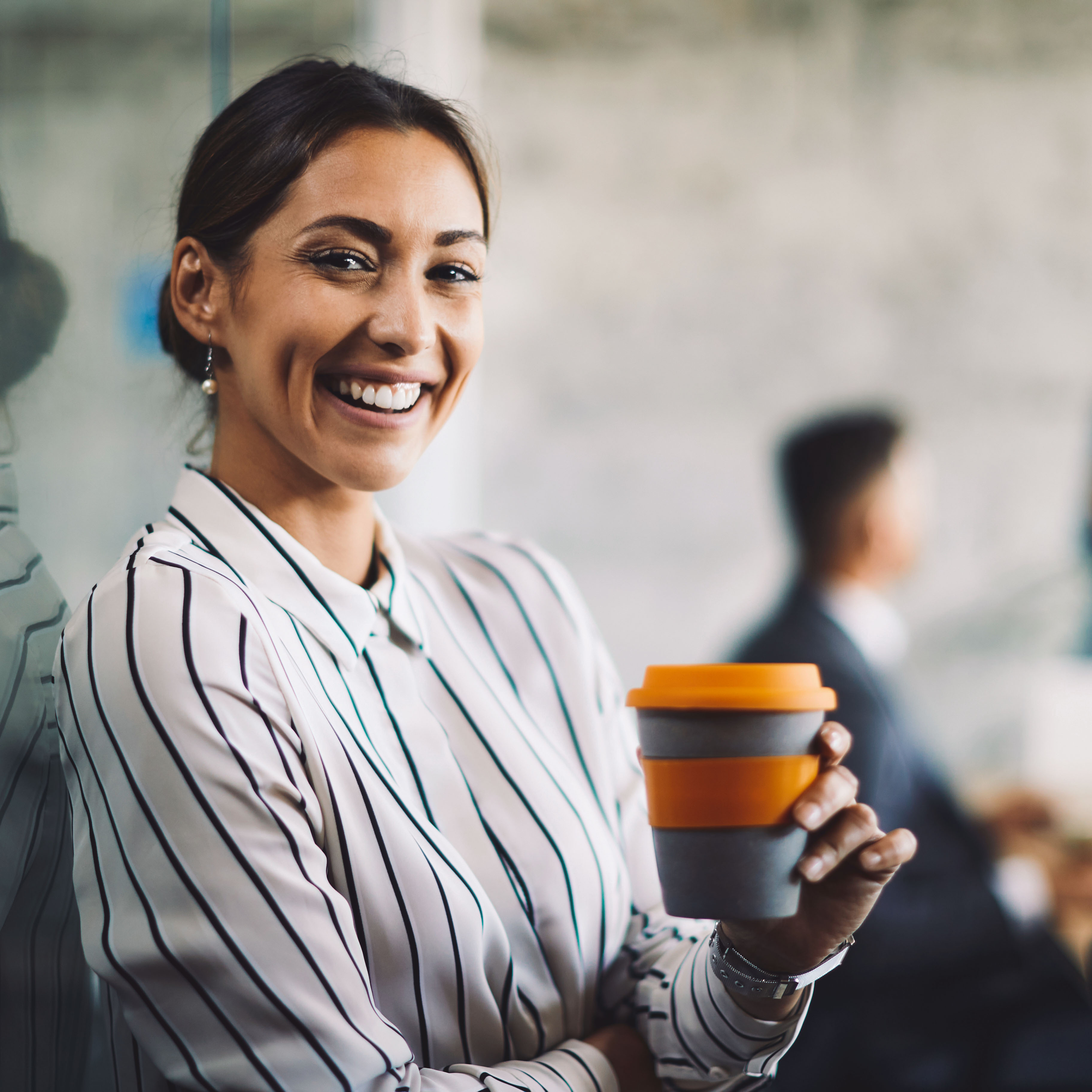 Cheerful woman holding orange coffee mugs in a workplace setting