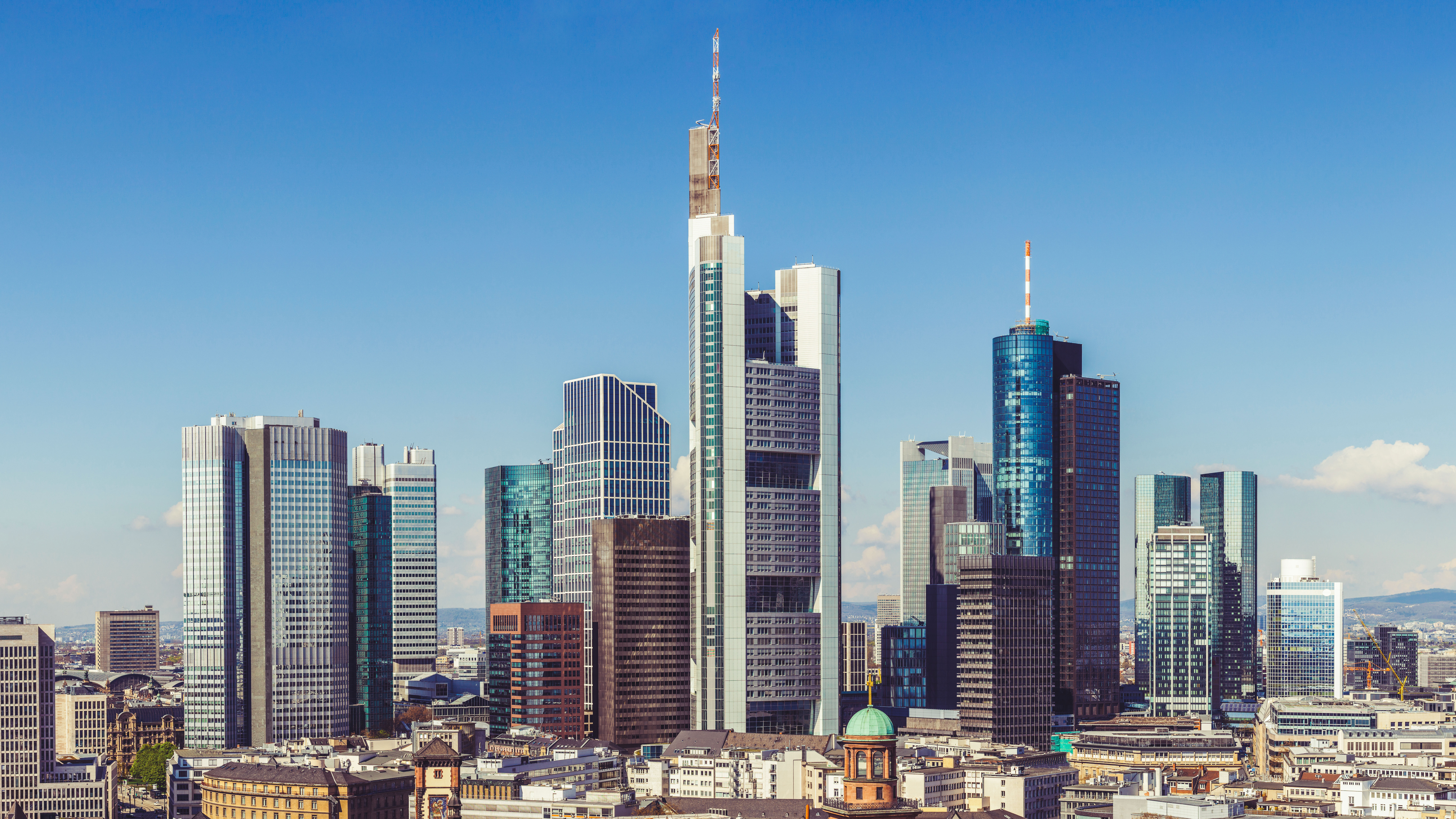 Daytime skyline of Frankfurt with modern skyscrapers under a mostly clear sky.
