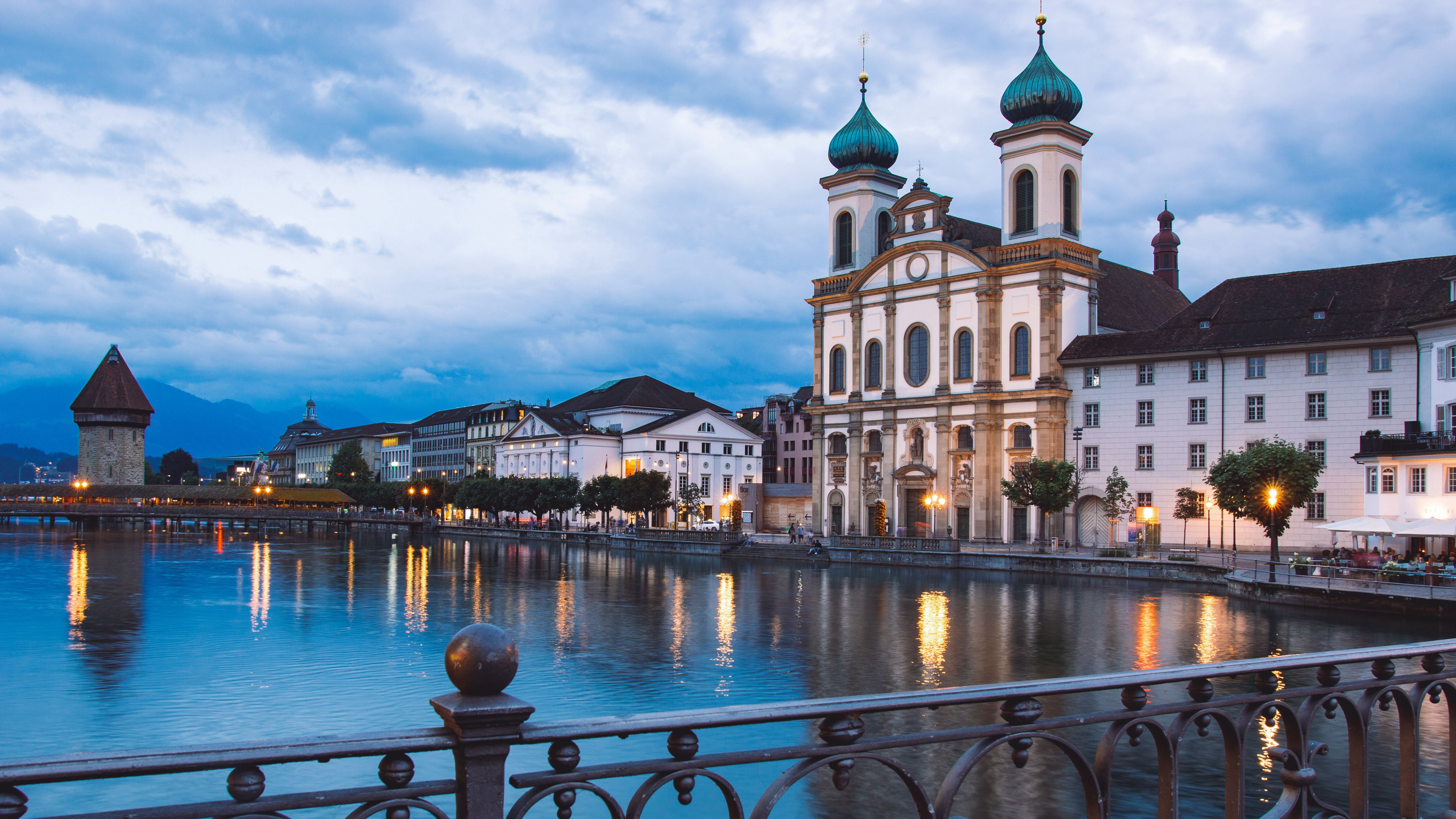 Evening view of Lucerne with historic buildings lining the edge of the lake, their reflections shimmering on the calm water.