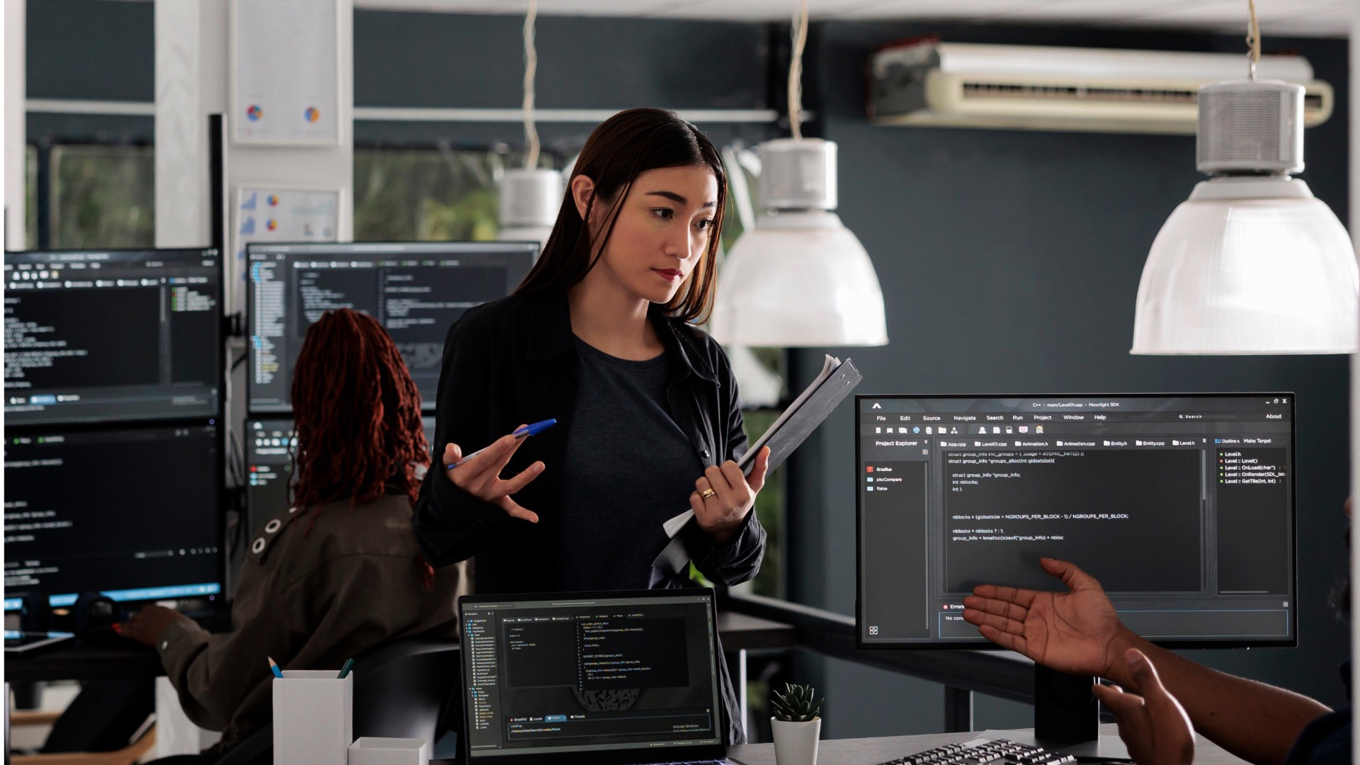 Woman discussing in front of multiple screens displaying software code in a modern office