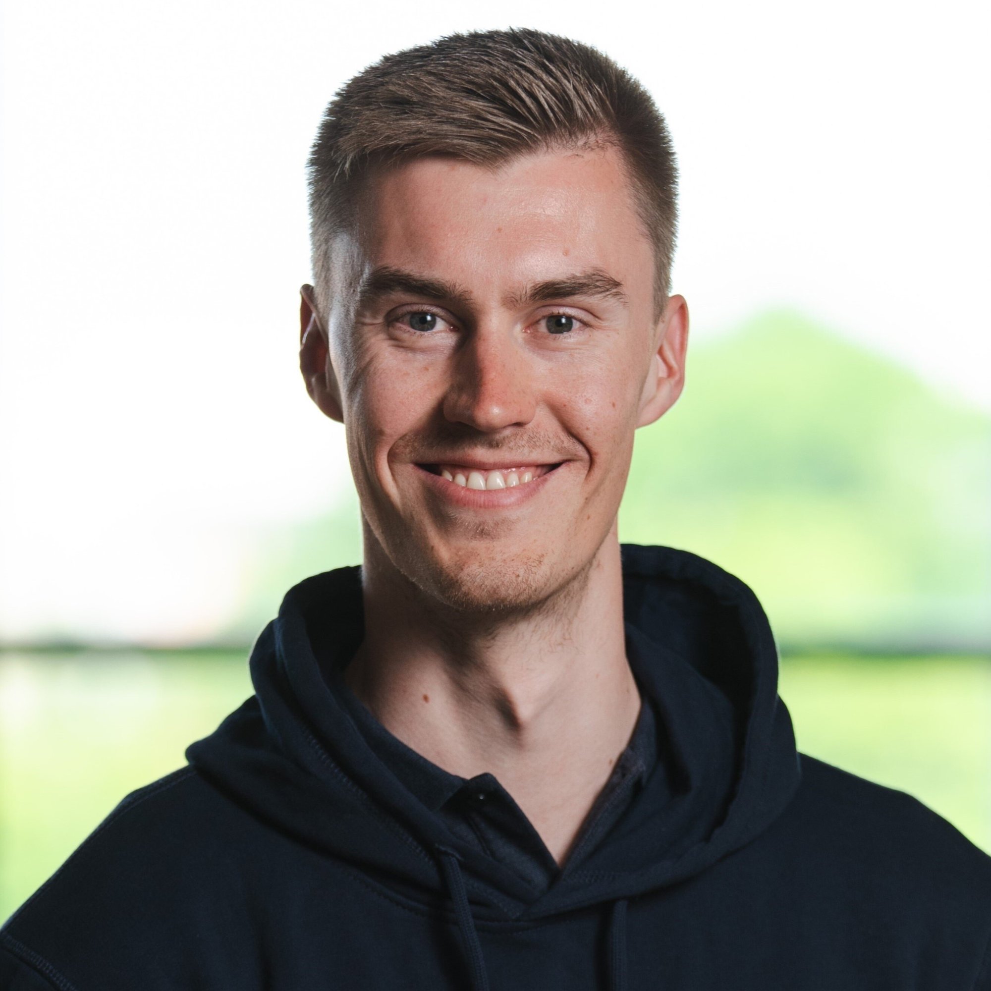 Jonne Kauko, smiling in a dark hoodie, in front of a bright, green-blurred background