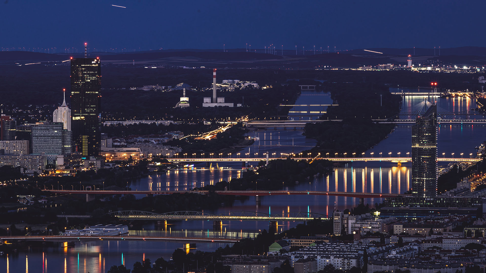 Evening aerial view of Vienna with the cityscape stretching toward the horizon and the river winding through the scene.