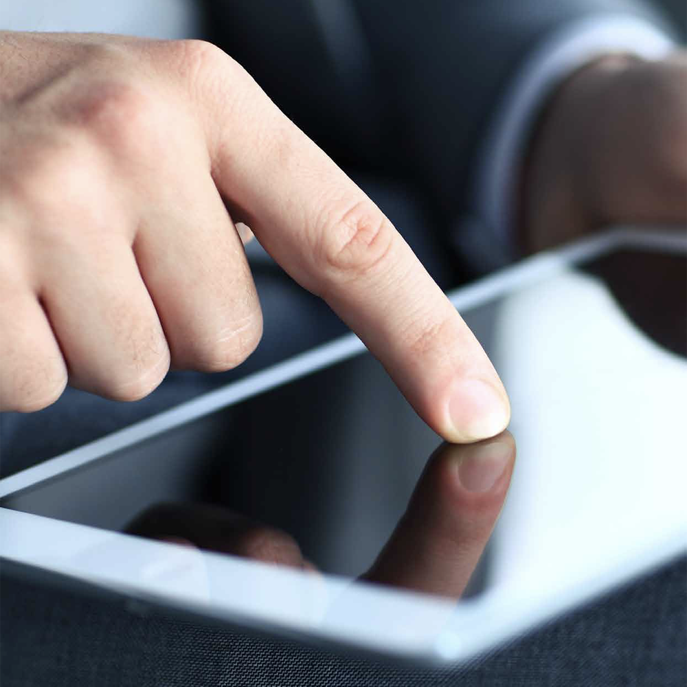 A finger in a suit touches the screen of a tablet or smartphone, whose surface reflects the image of the finger.
