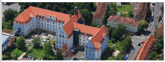 Aerial view of the Würzburg District Office in daylight, surrounded by green spaces and roads.